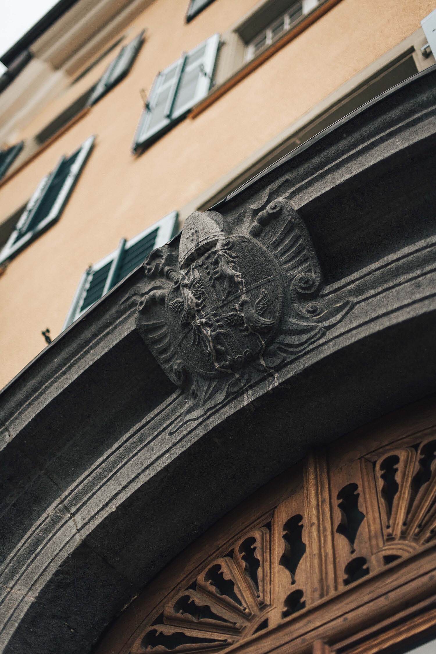 A close-up of an ornate stone archway with an eagle emblem above a carved wooden door.It's the entrance to the historic Hotel Palais Bad Ragaz.