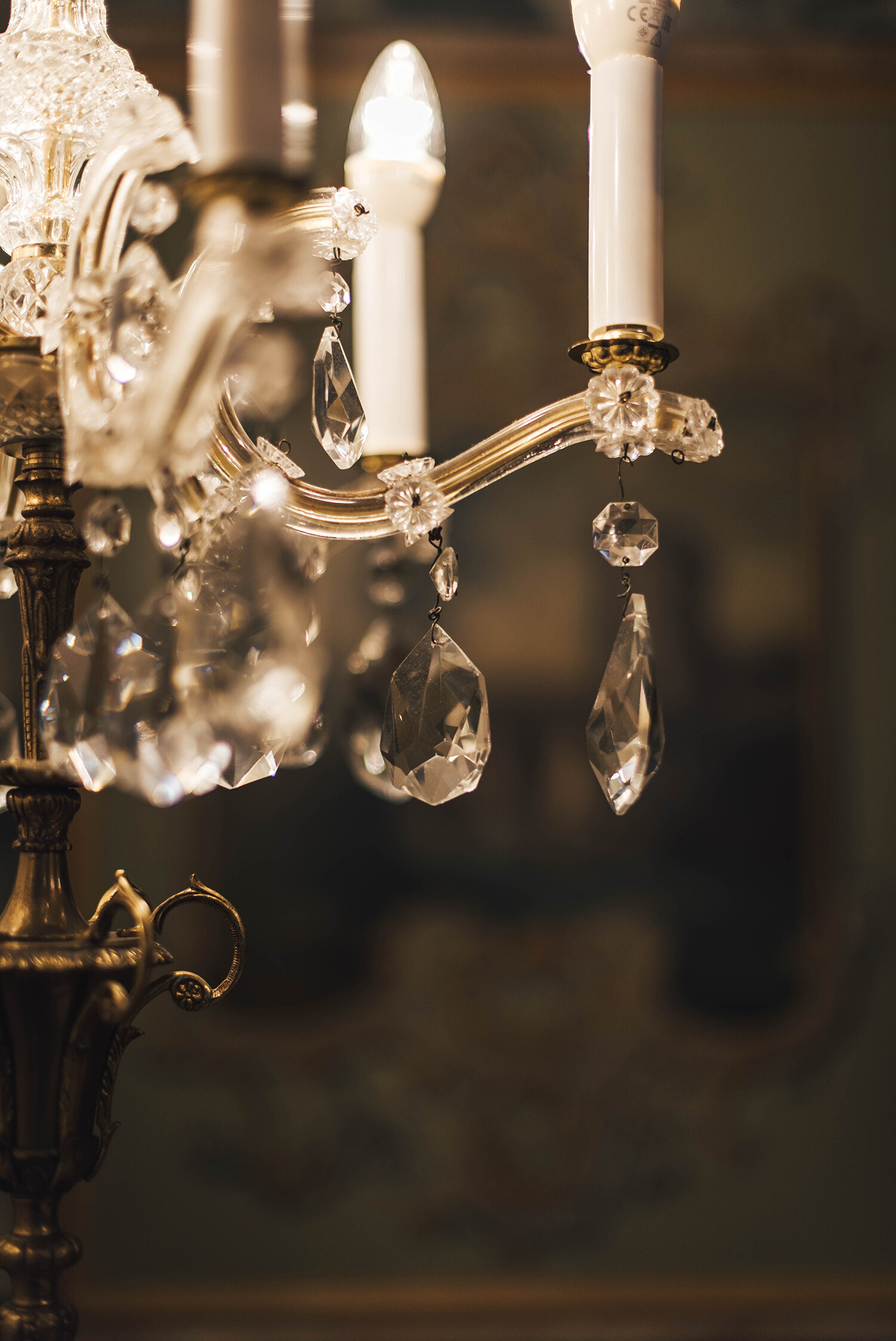 Close-up of an ornate chandelier from the hotel Palais Bad Ragaz with crystal pendants and white candle-shaped bulbs, set against a blurred, warm-toned background.