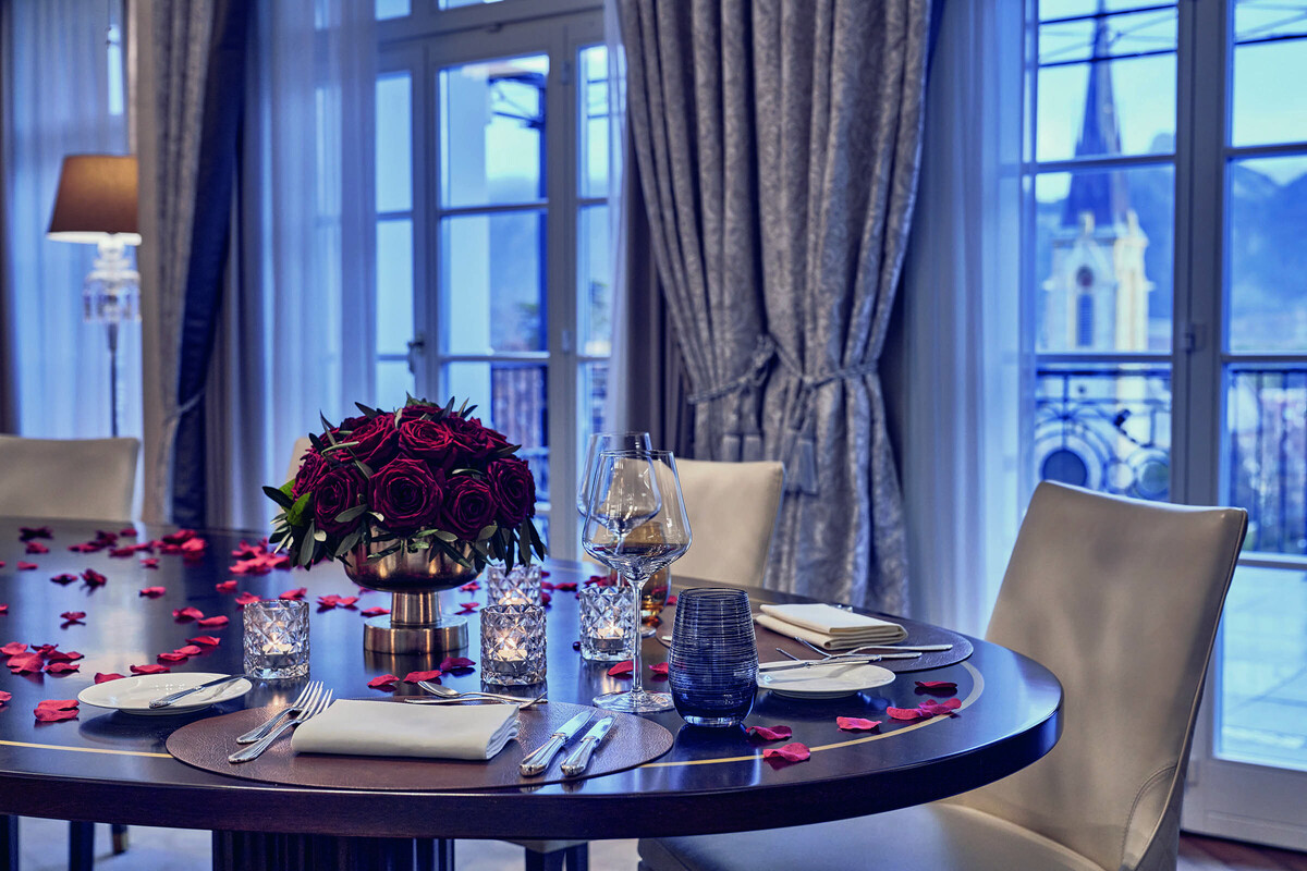Elegant dining room with a round table set for two, featuring red roses and petals.