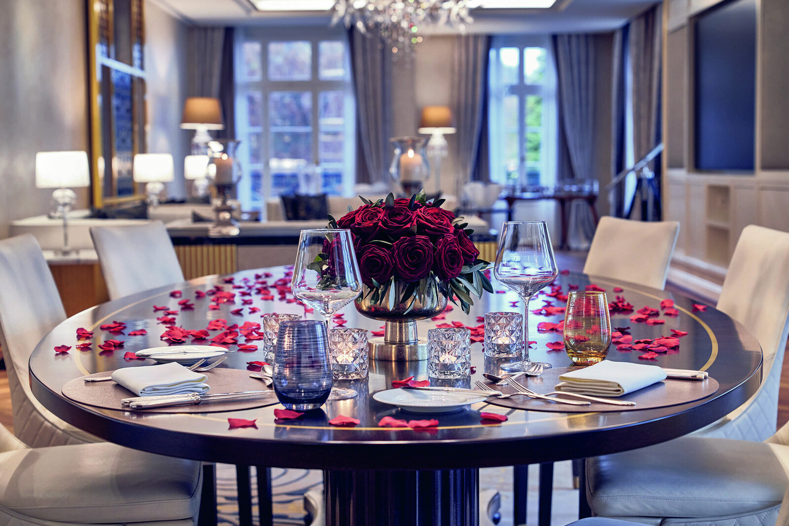 Ein eleganter Esstisch, gedeckt mit einem Strauß roter Rosen, umgeben von Rosenblättern, Gläsern und Kerzen, schafft ein romantisches Ambiente in einem sanft beleuchteten Raum.