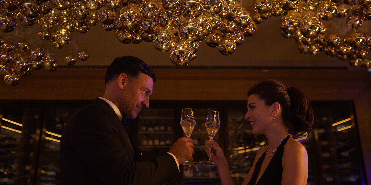 Ein Paar schaut sich tief in die Augen und stösst in romantischem Ambiete an.