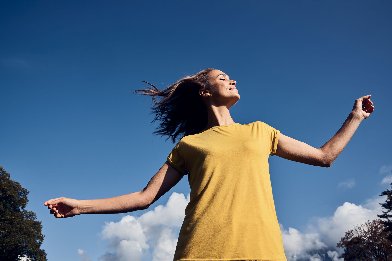 Glückliche Frau in gelbem Sommerkleid tanzt in der Natur